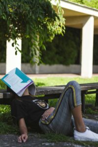 Girl sitting on school campus, leaning against bench with a book lying open, facedown on her face