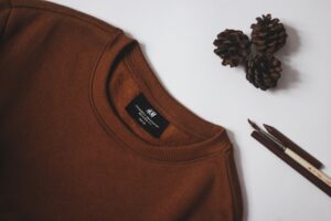 Brown Sweater on a white table with pinecones, and drawing utensils next to it