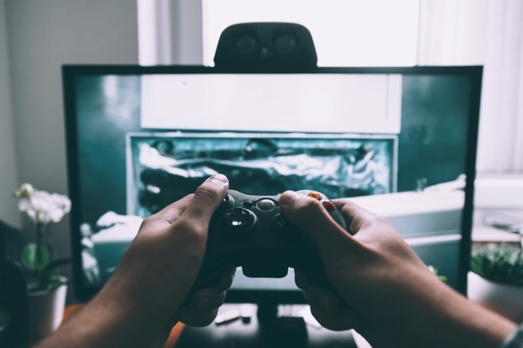 A person using a gaming controller in front of a monitor