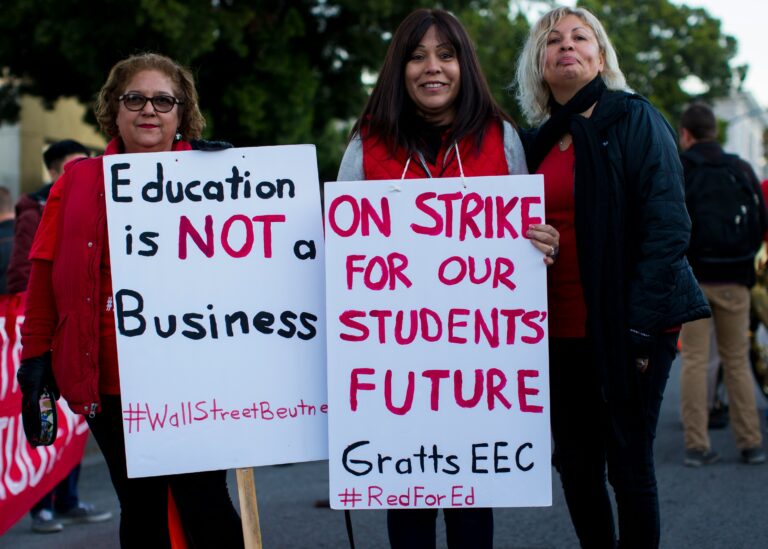 3 teachers holding poster about teacher strike that says "Education is NOT a Business" and "ON STRIKE FOR OUR STUDENTS' FUTURE Gratts EEC #RedforEd"