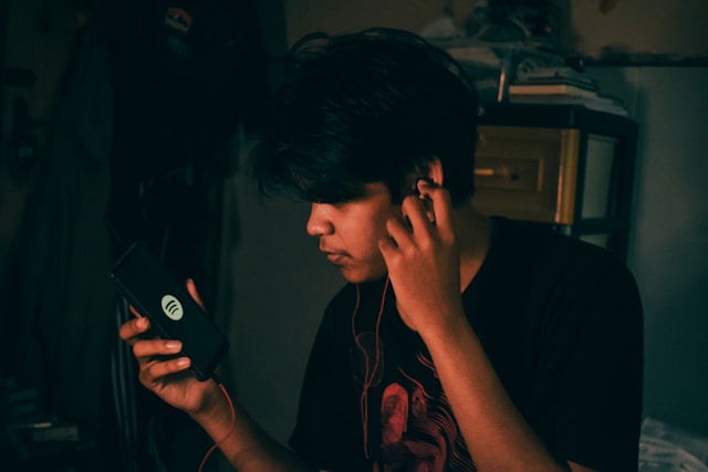 A person listening to music through headphones while checking their phone in a dimly lit room.